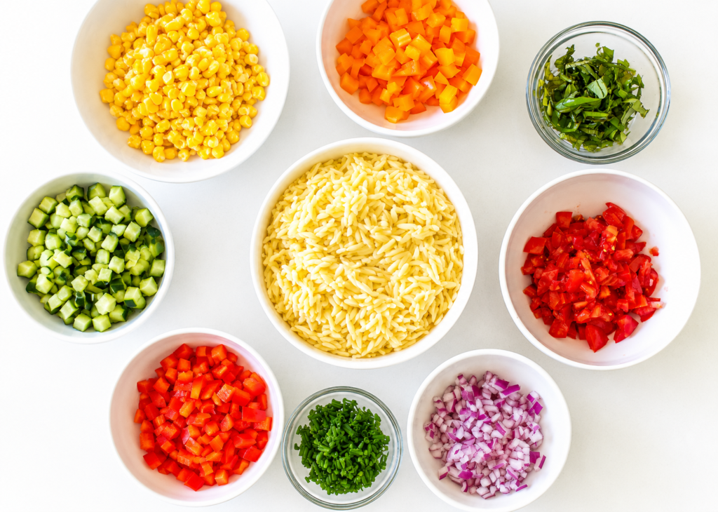 Bell peppers, corn, cucumber, and tomatoes combined with orzo in a bowl
