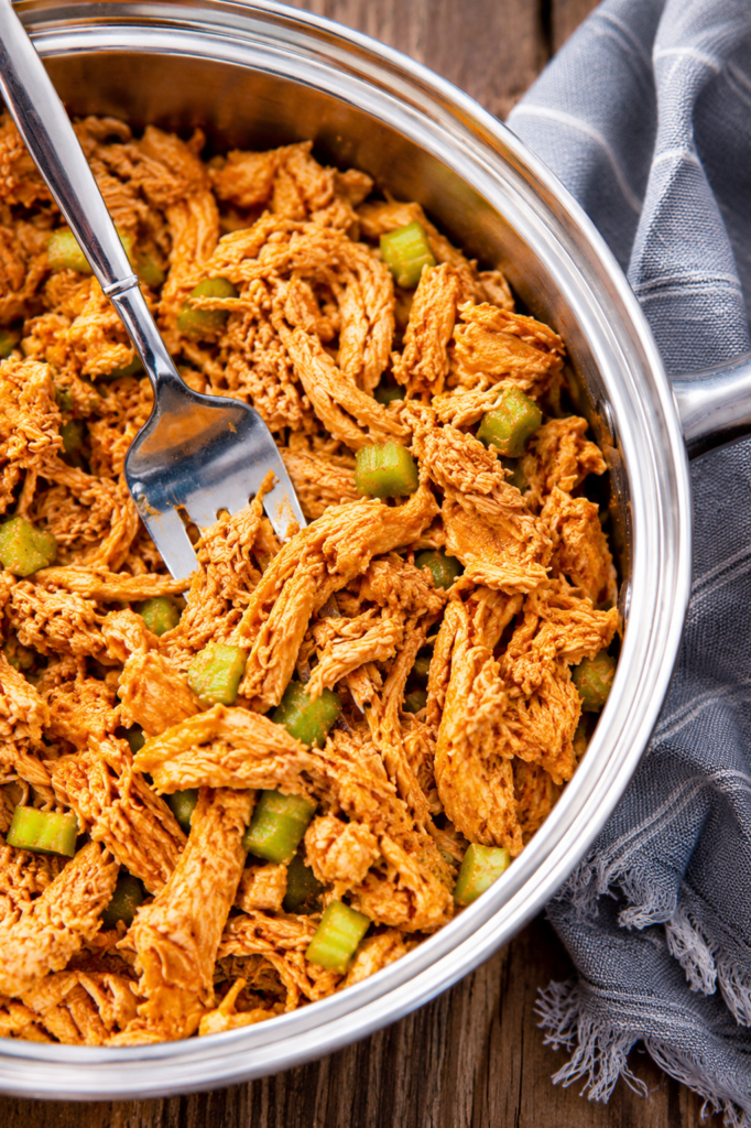 Hot sauce being stirred into shredded chicken with butter